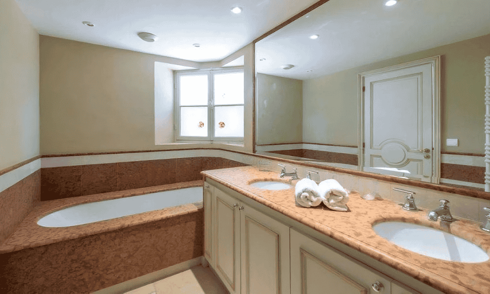 En suite bathroom at Villa Cap d’Antibes with dual marble sinks, built-in bathtub, and mosaic tile surround under recessed lighting