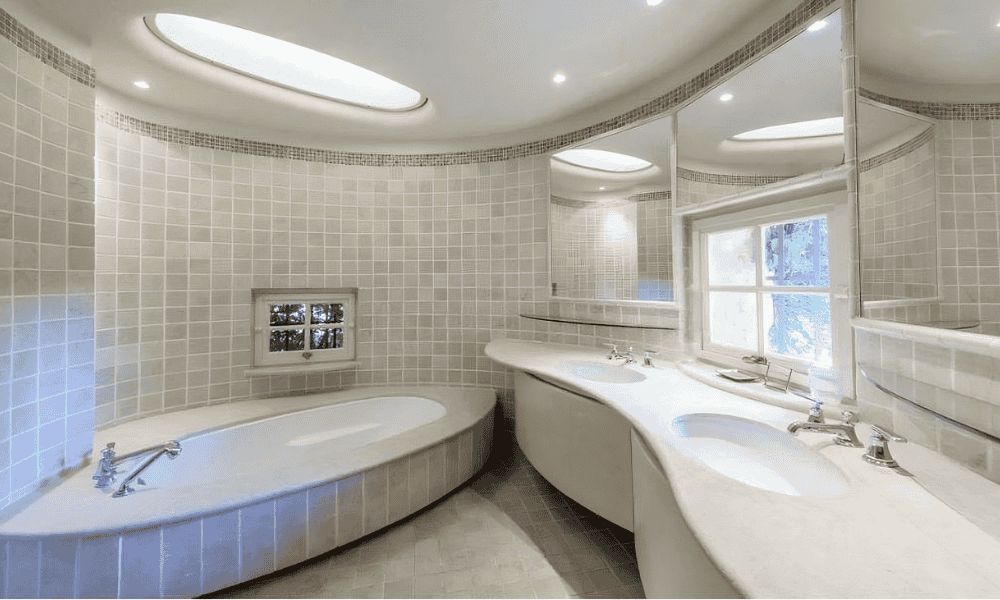 Curved en suite bathroom at Villa Cap d’Antibes featuring mosaic-tiled walls, a built-in tub under a skylight, and a curved double vanity