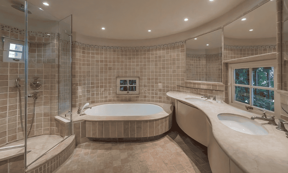 En suite bathroom at Villa Cap d’Antibes featuring a curved glass shower, built-in bathtub, and a double vanity with a window view