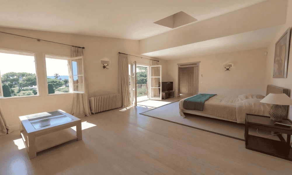 Spacious bedroom at Villa Cap d’Antibes with a king-size bed, low coffee table, and large windows opening to garden views