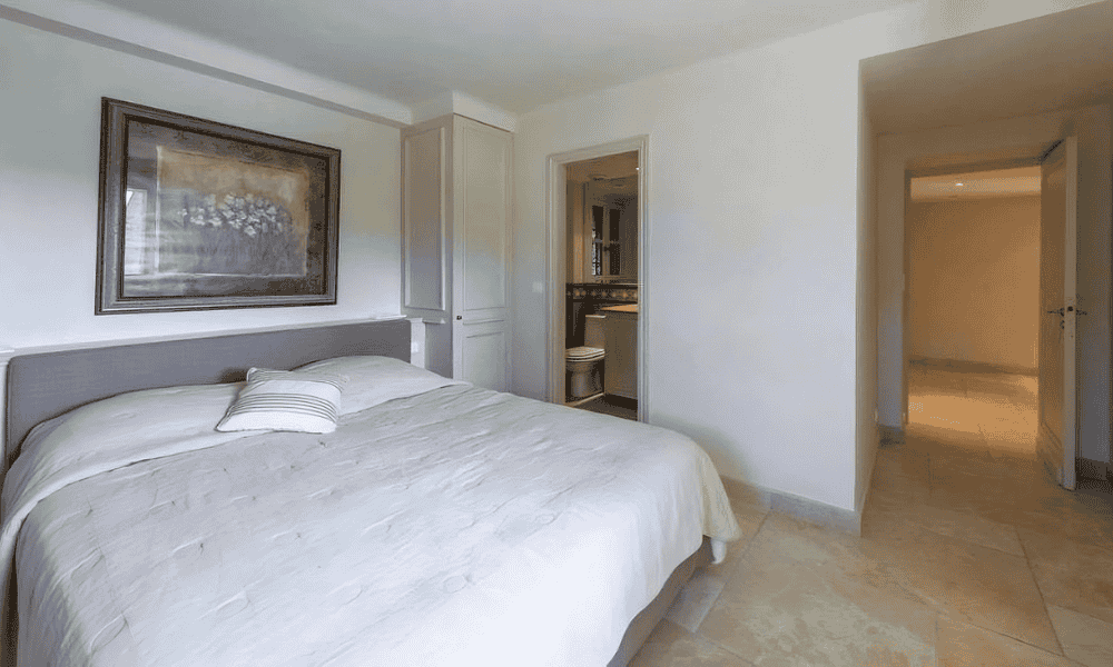 En suite bedroom at Villa Cap d’Antibes with a white bed, framed artwork, and an open door revealing the adjoining bathroom