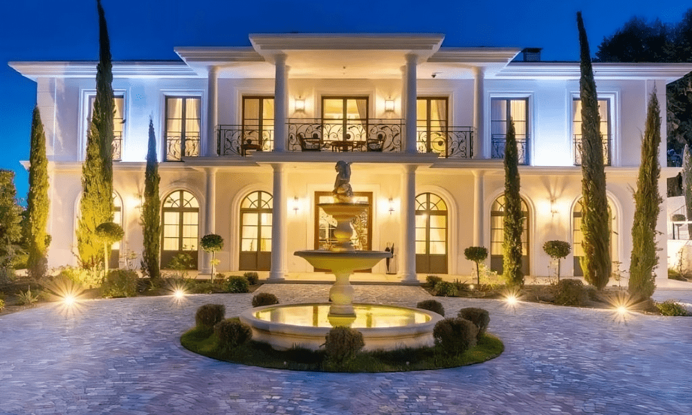 Aerial exterior view of a contemporary luxury villa with floor-to-ceiling glass, infinity pool, and Mediterranean hillside backdrop