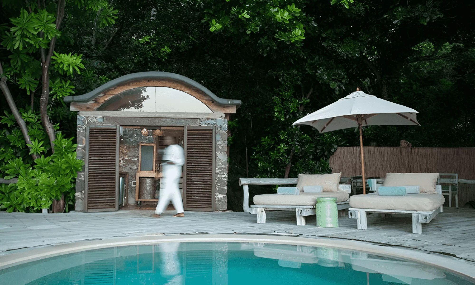 Circular pool with sun loungers and a waiter in the background.
