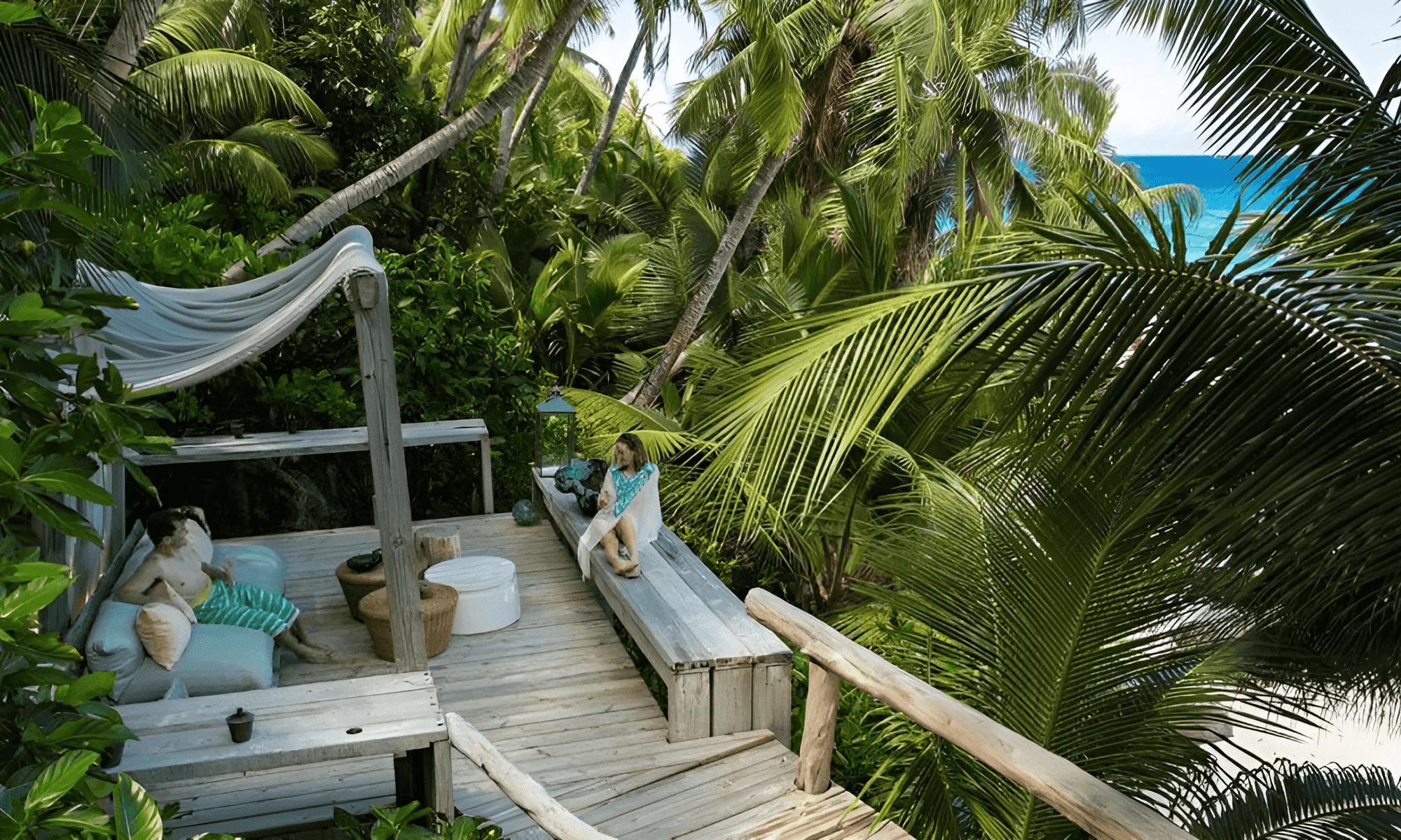 People relaxing on the terrace of the pool surrounded by palm trees.