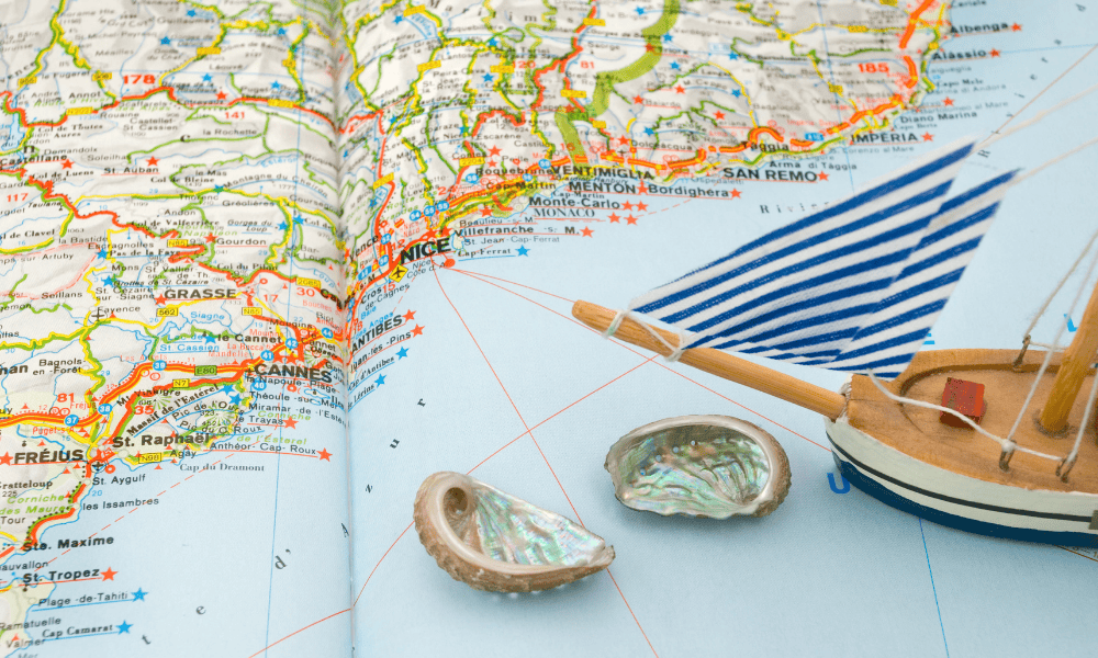 Vintage map of the French and Italian Riviera with a model sailboat and seashells illustrating Villa Hotels’ exclusive destinations