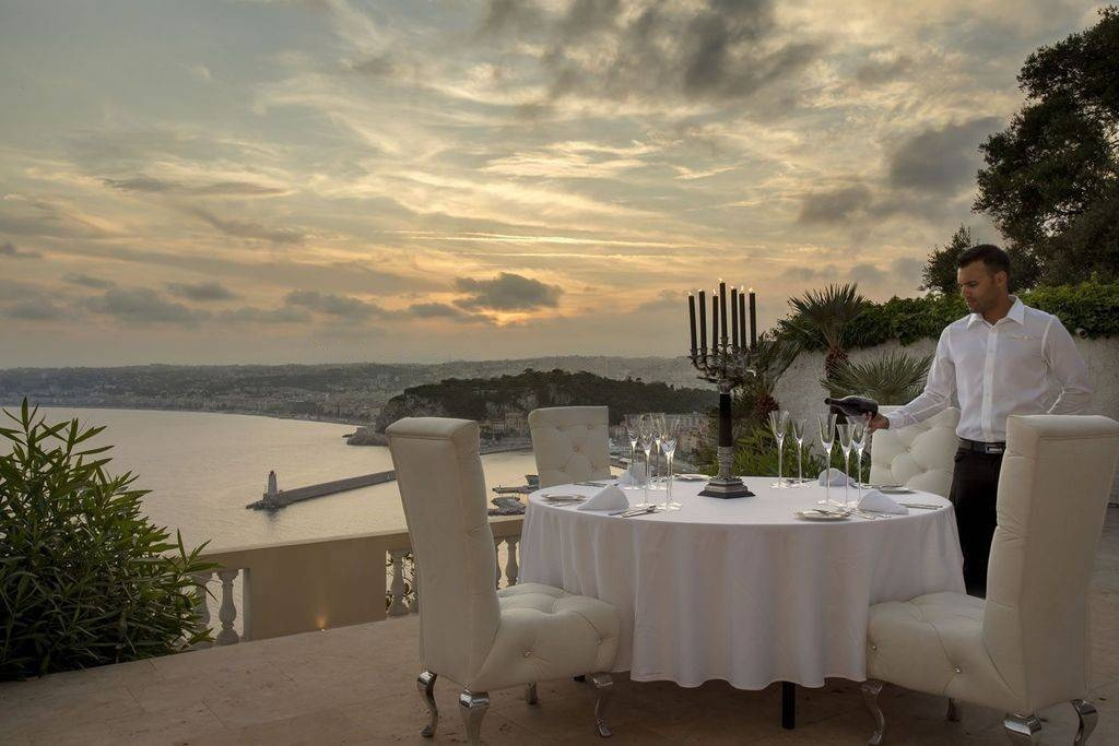 Waiter pouring fine wine at an elegantly set outdoor terrace table with panoramic ocean views at sunset