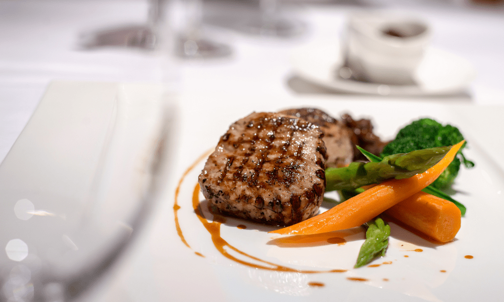 Grilled pork chop with glazed carrots, asparagus tips, and broccoli florets drizzled with pan jus on a rectangular plate
