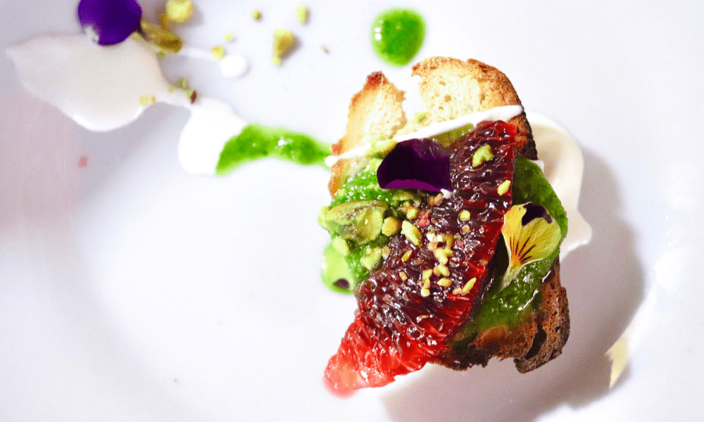 Blood orange carpaccio on toasted brioche with pistachio crumble, edible flower petals, and yogurt drizzle