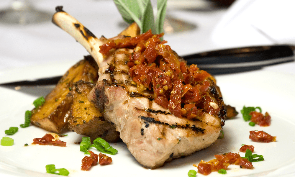 Grilled bone-in chop topped with sun-dried tomato relish, served with seasoned potato wedges and chopped scallions