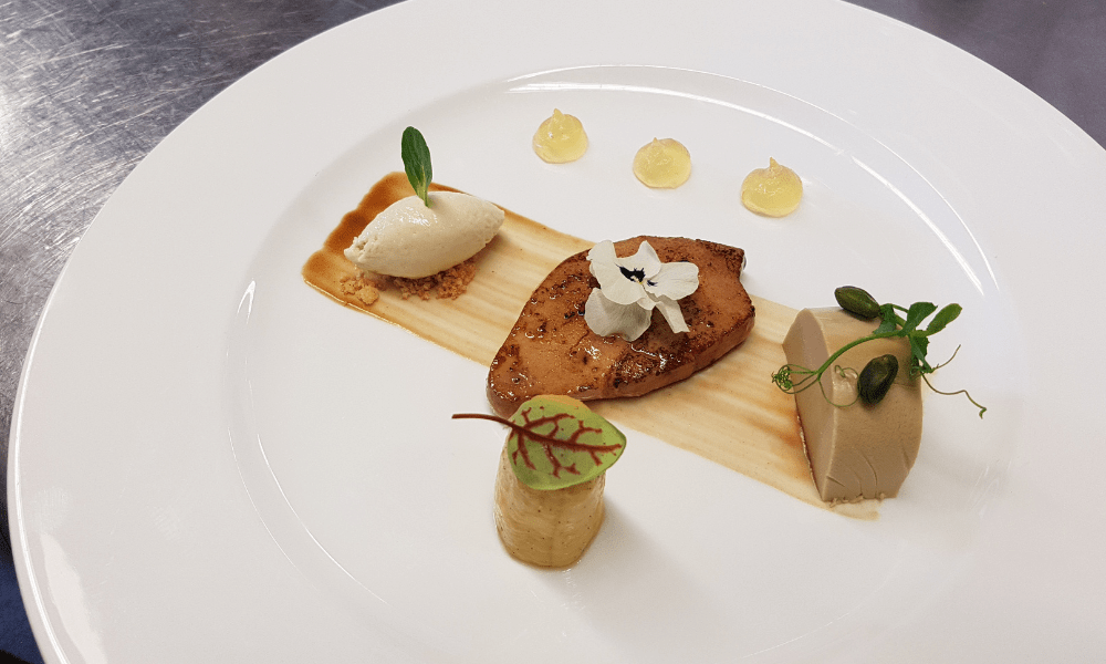 Seared foie gras garnished with edible flower, served alongside coffee panna cotta, ice cream quenelle, nutty cylinder, and lemon gel dots