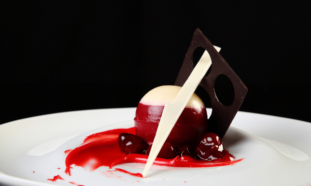 Red and white chocolate mousse sphere on cherry coulis, adorned with geometric dark and white chocolate accents