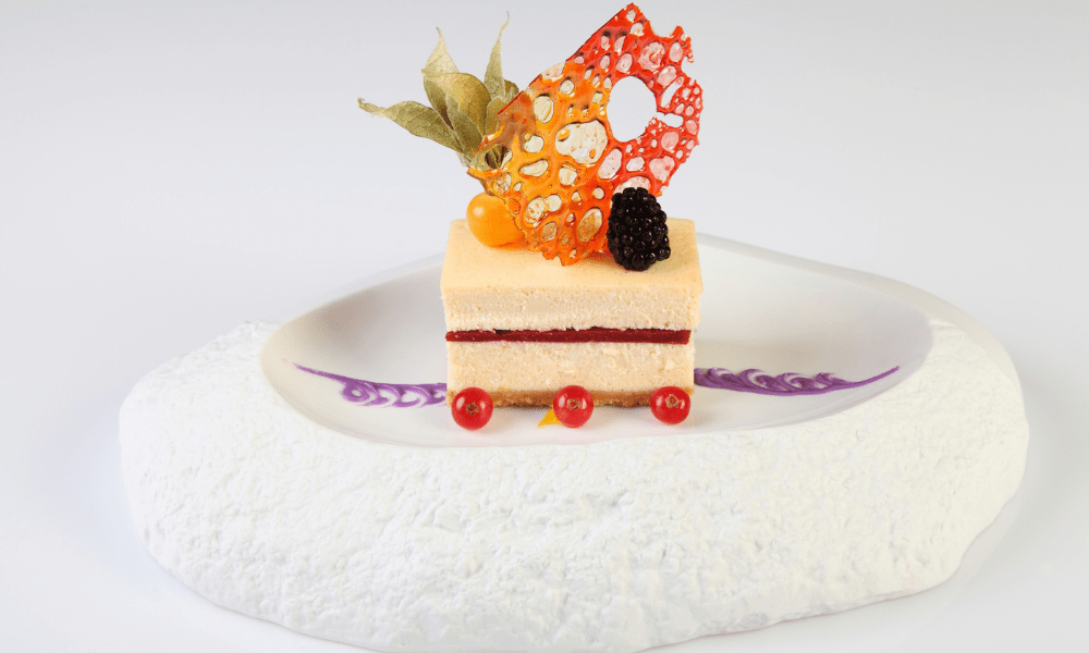Layered raspberry mousse cake with caramelized sugar tuile, physalis berry, fresh blackberry, and redcurrants
