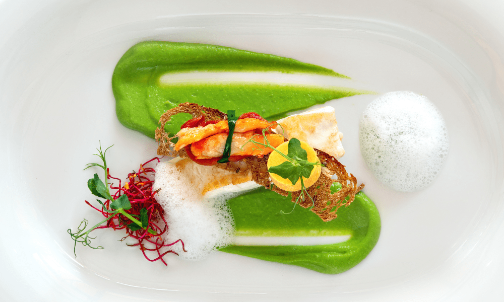 Lobster tail wrapped in chive, presented on green pea purée with culinary foam, crispy bread lattice, and microgreens