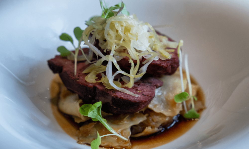 Roasted venison slices over handmade ravioli, topped with sauerkraut and microgreens in a rich game jus