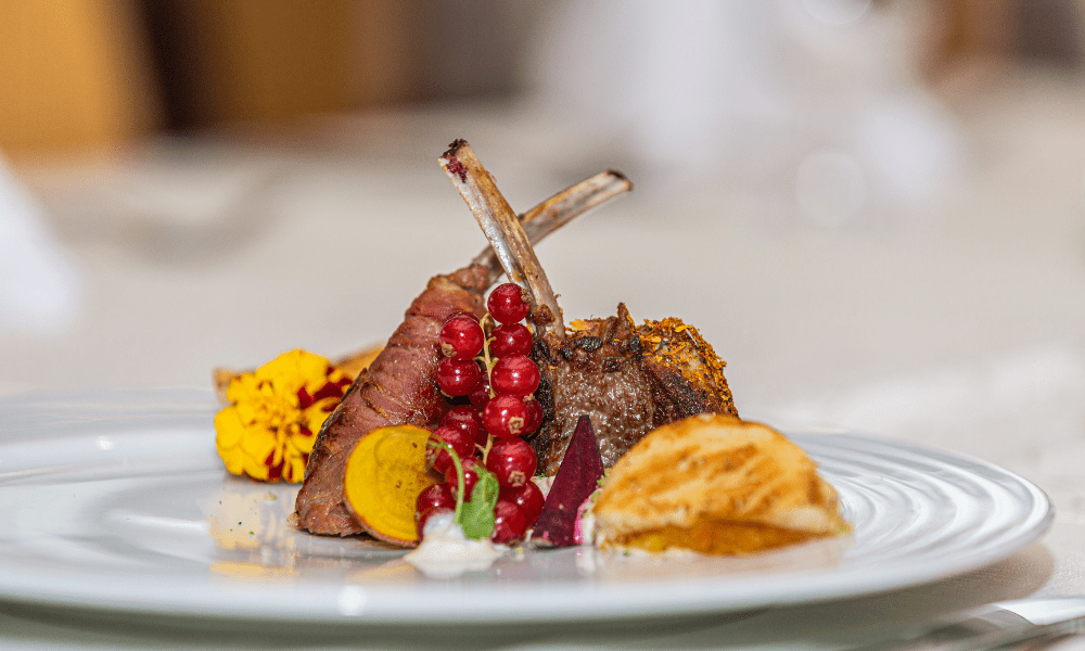 Grilled lamb chop lollipops with redcurrants, heirloom beet slices, golden beetroot, and a potato rosette on a fine porcelain plate