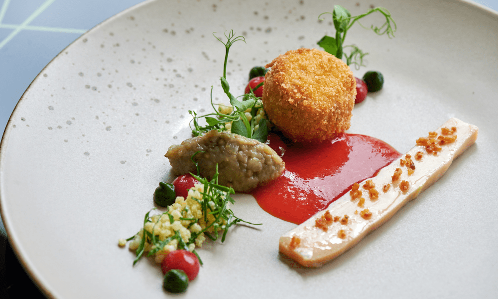 Crispy panko croquette on red pepper coulis, served with eggplant purée, pea tendrils, and micro herb sprigs
