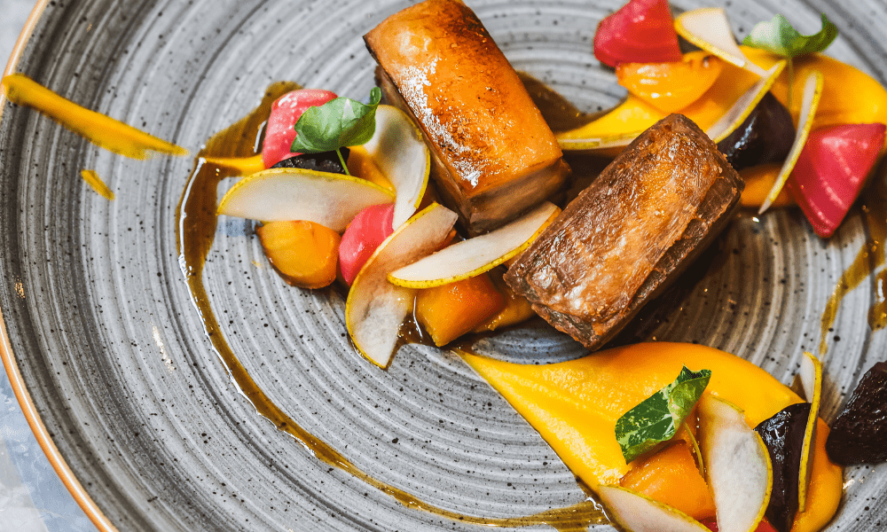 Braised beef ribs with carrot purée, thinly sliced pear, pickled beetroot, and fresh herb garnish on a stoneware plate