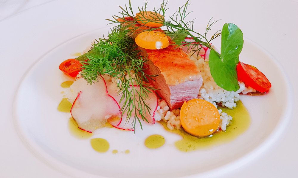 Pan-seared duck breast with pearl barley, golden cherry tomatoes, radish slices, and dill oil drizzle on a white plate