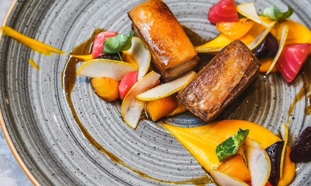 Gourmet dish of seared pork belly with colorful vegetable garnish and artful sauce presentation