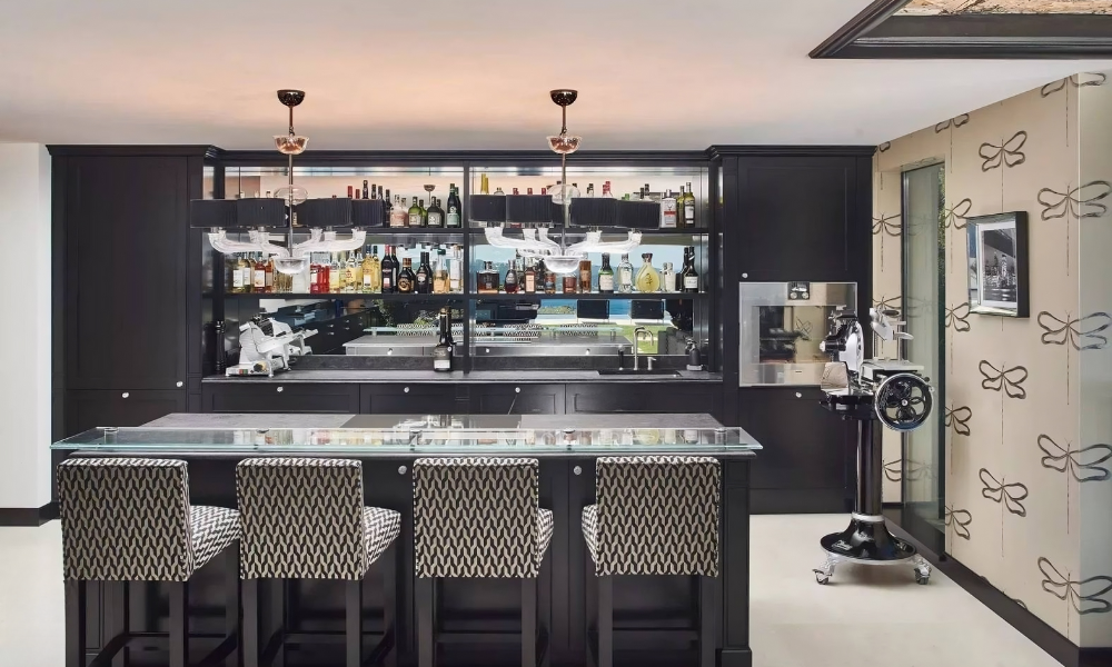 Elegant villa bar with glass-topped counter, patterned stools, and backlit shelves of premium spirits