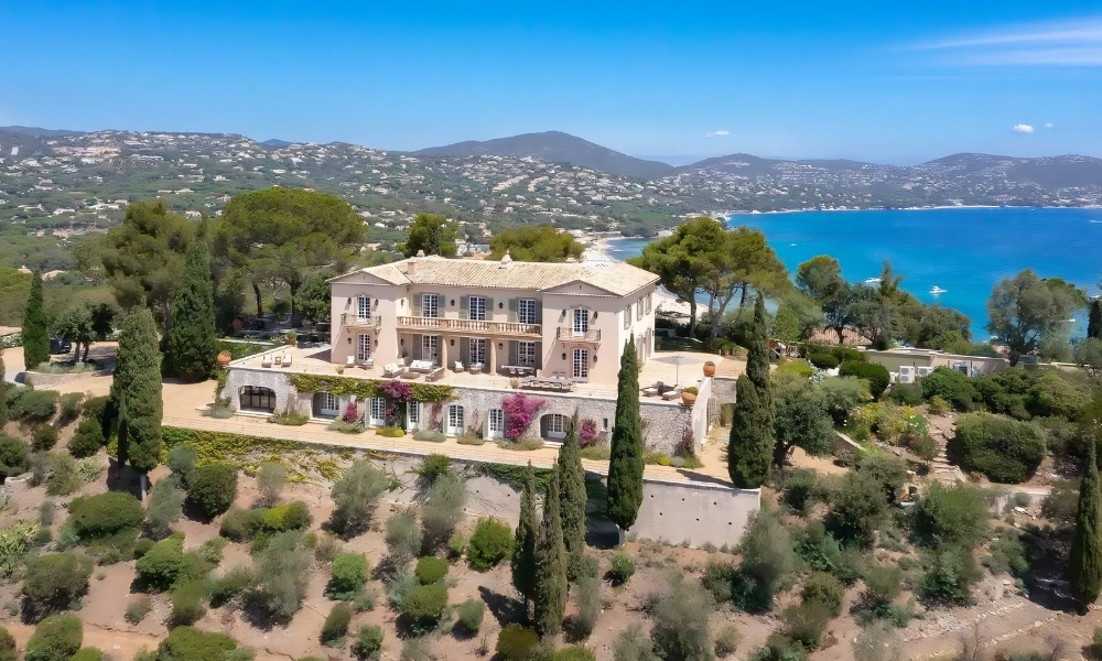 Panoramic aerial view of a Provençal villa perched on olive-and-cypress hillside with the Mediterranean Sea beyond