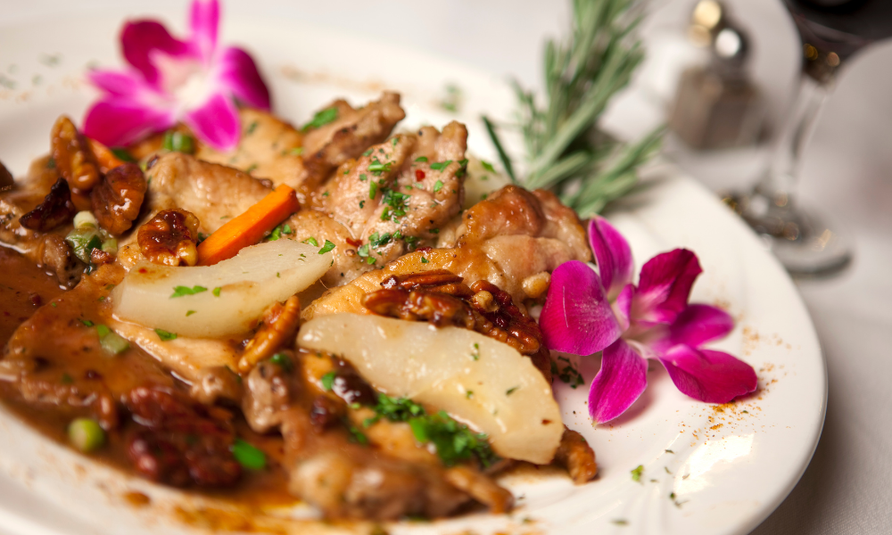 Seasonal meat ragout with pear slices, caramelized pecans, and an edible orchid garnish on a white plate