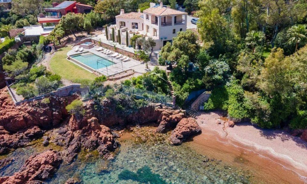 Cliffside villa above a red-rock beach, featuring an infinity pool and lush Mediterranean foliage