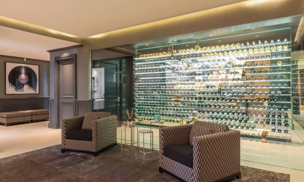 Luxury lounge with patterned armchairs and a glass-enclosed, backlit wine display wall